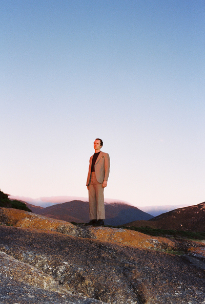 Darvid Thor is standing on a rocky surface in front of a view of dark mountains against a hazy blue sky.