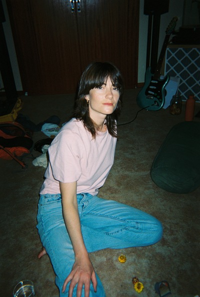 Rowena Wise is sitting on the floor in a dark room, looking straight at the camera.